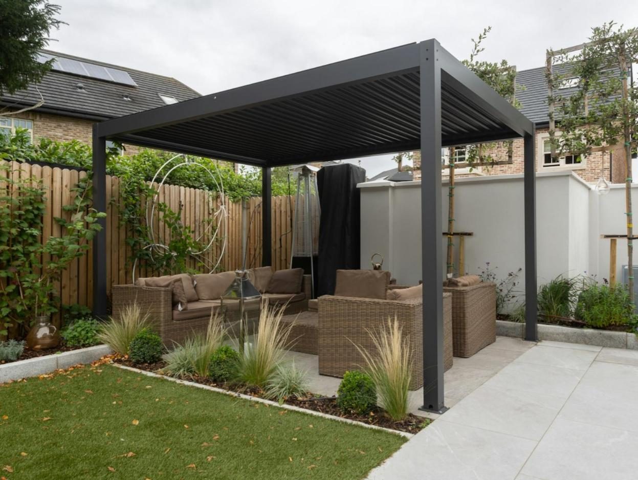 Black aluminum louvered roof over outdoor sofas in a fenced garden