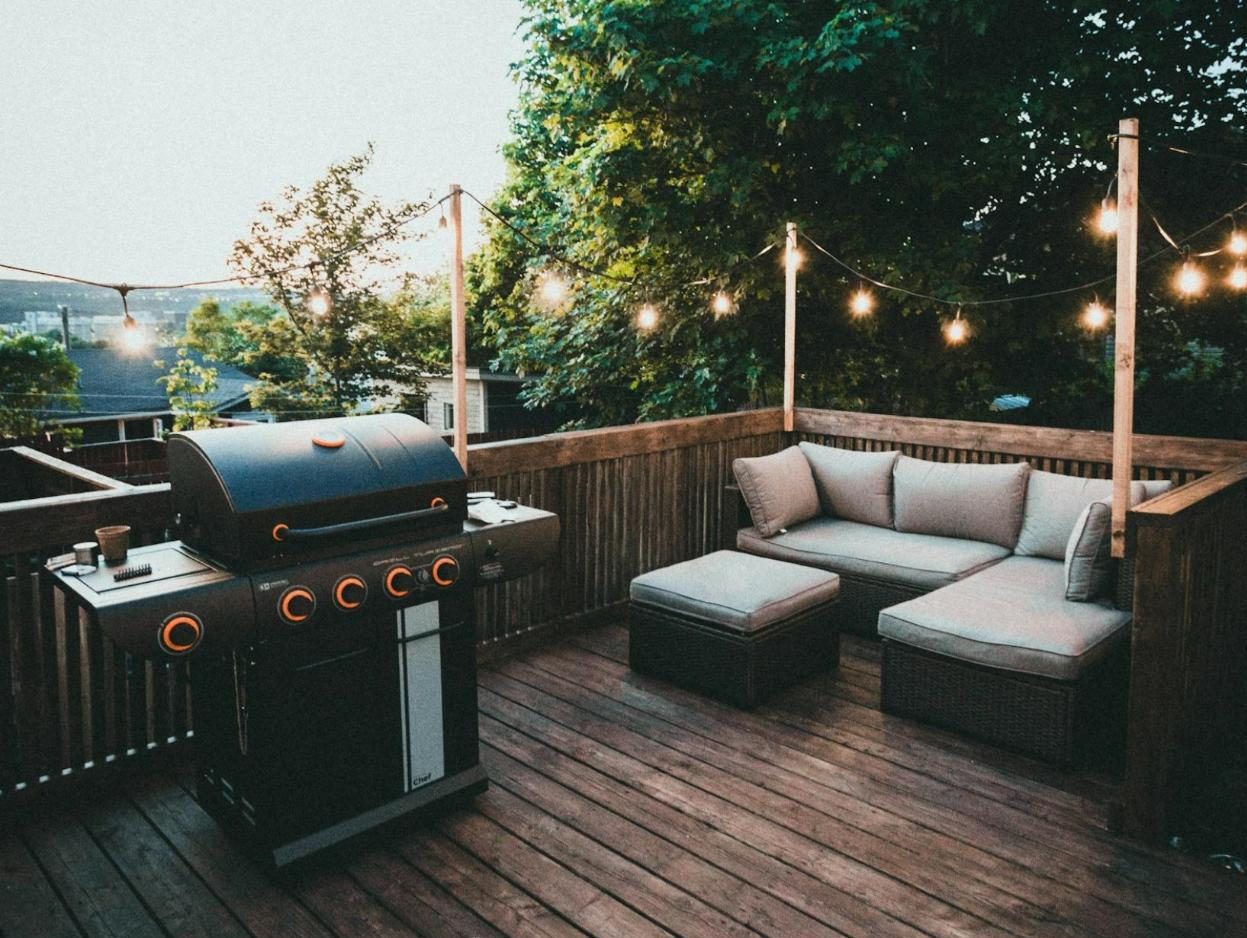 Dark-stained deck with a grill, outdoor sectional and string lights